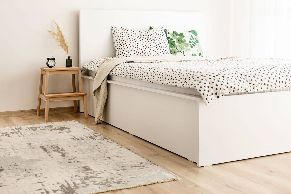 A white bed with a solid storage base and polka dot bedding, a wood step stool beside it as a nightstand