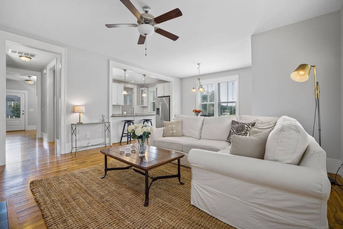A living room with a white slipcovered sofa and a coffee table on a jute rug, and a hallway to a glass-paneled door