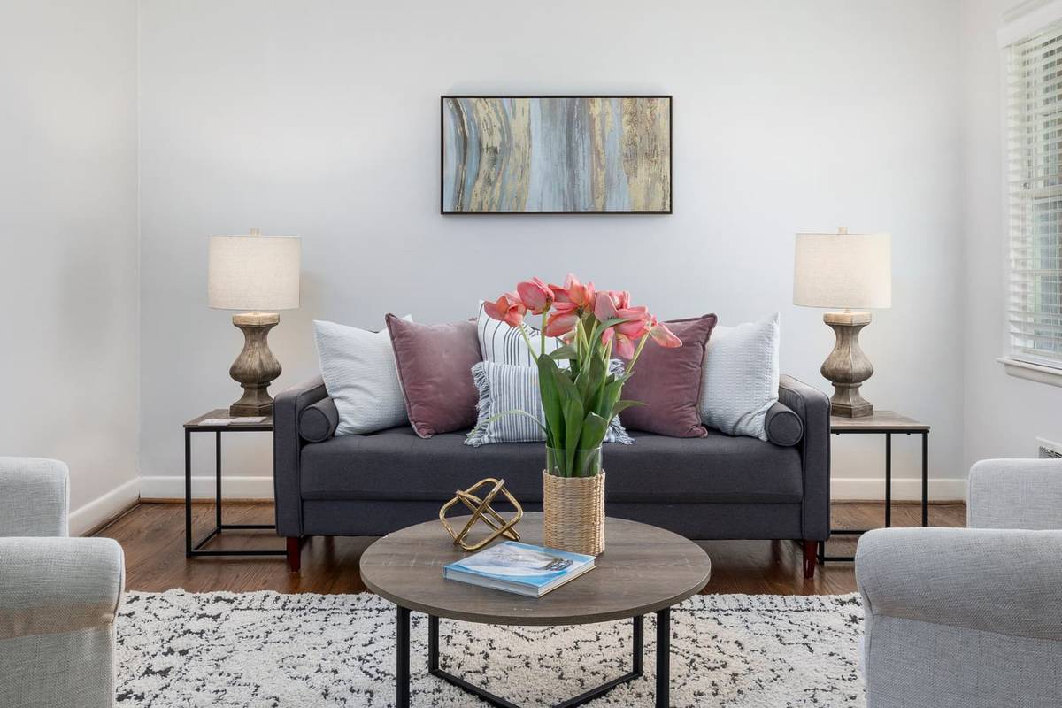 A charcoal sofa centered on a white wall under an abstract print, between two side tables with matching lamps