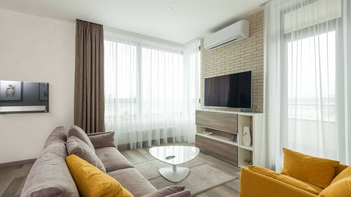 A TV mounted on a brick wall above a wood media console, across from a gray sofa and a yellow armchair