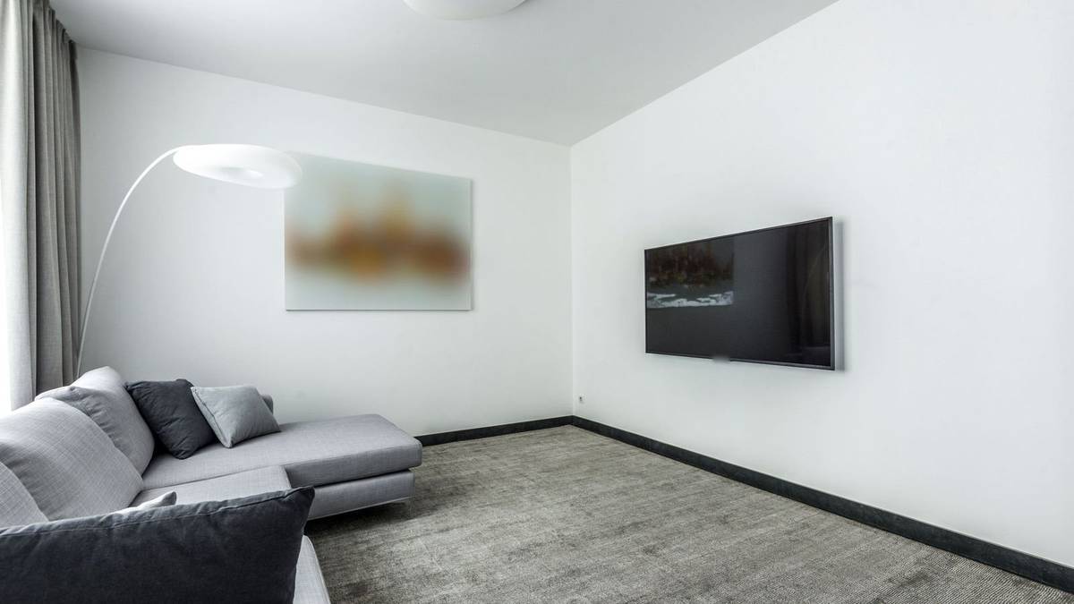 A TV mounted low on a white living room wall across from a gray sectional sofa