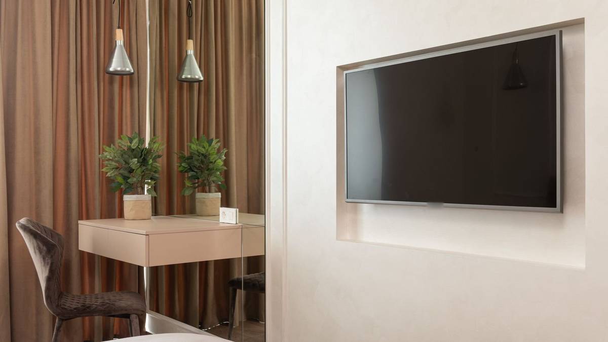 A TV mounted in a shallow wall niche, beside a small desk under two pendant lights