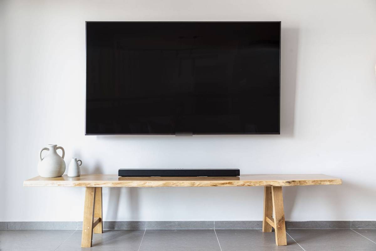 A flat-screen TV mounted on a white wall above a long wooden console