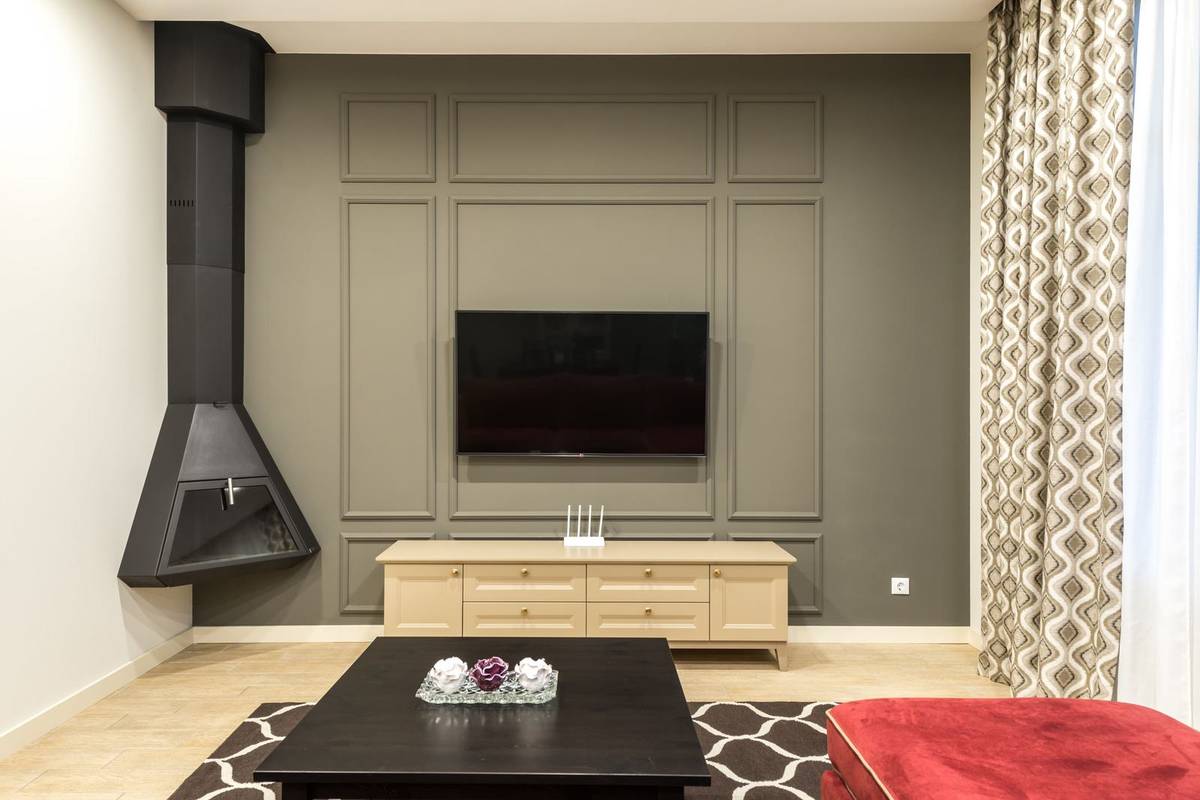 A TV on a dark gray paneled accent wall above a low wood console, with a black hanging fireplace in the corner