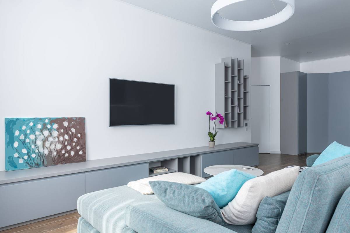 A white living room with a TV mounted above a long, low gray console, facing a light blue sofa
