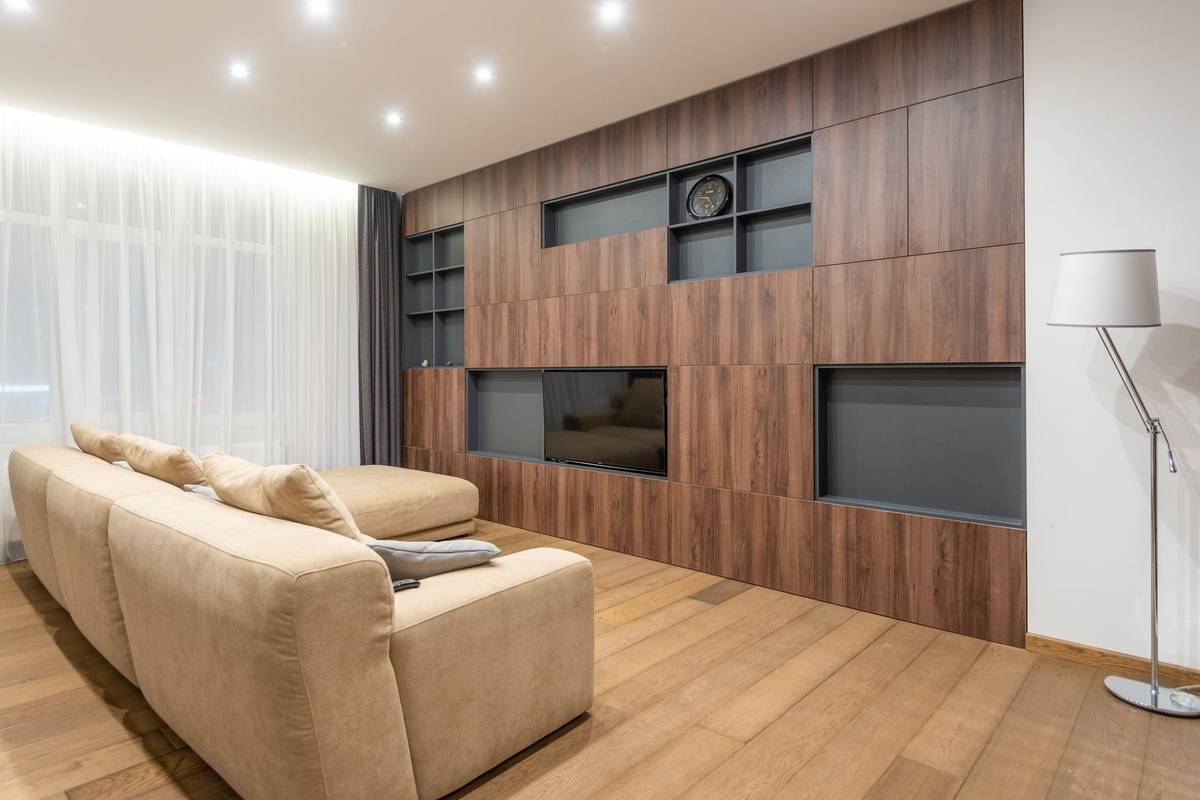 A wood media wall with built-in shelves and open niches around a recessed TV, facing a beige sectional