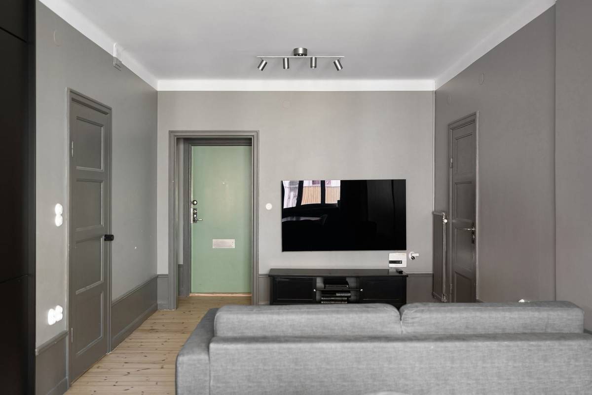 A small gray living room with a TV mounted over a low black stand and a gray sofa a short way in front