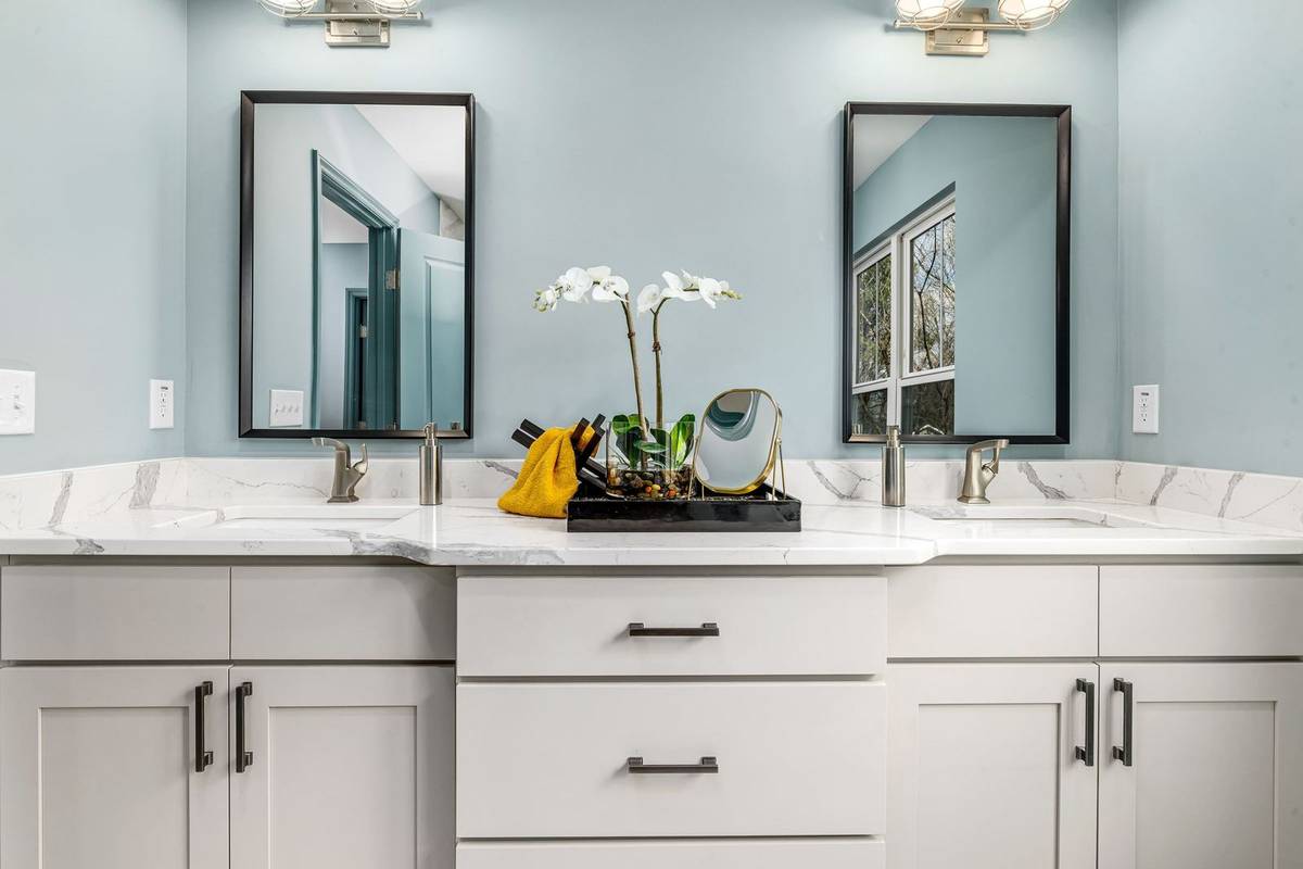 A white double vanity with two black-framed mirrors, each centered over its sink, and a light fixture above each mirror