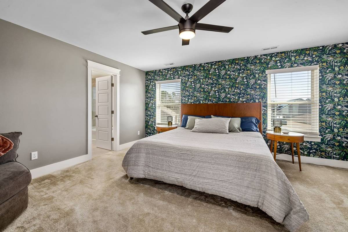 A bedroom with a dark green botanical wallpaper accent wall behind the bed and round wooden nightstands